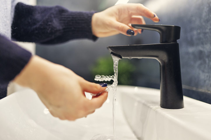 The girl is washing her transparent dental aligner before wearing it.